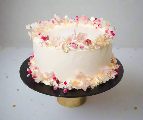 White cake with floral decorations on a black cake stand against a white background