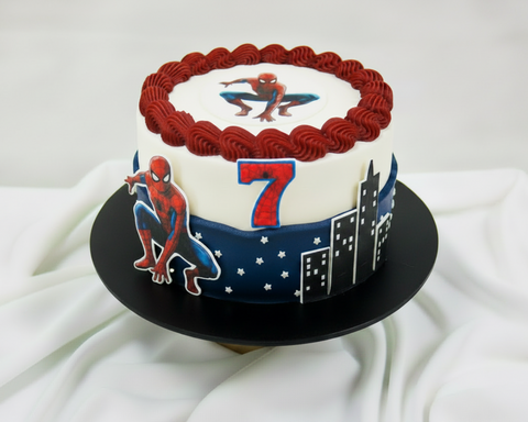 A round frosted Spider-Man Birthday cake on a black cake board, decorated with a white top section, dark red piped rosette border, dark blue lower band, and a Spider-Man graphics on the centre top and on the body of the cake.