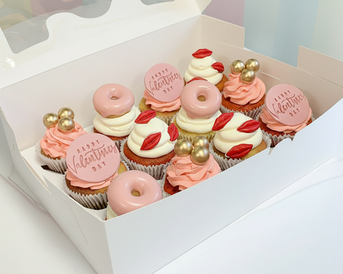 a box of 12 Valentine cupcakes. Share the love and make it sweet with this well thought out cupcake treat box. This year you can send chocolate lip kisses, golden chocolate balls, pink donut holes and "Happy Valentine" messages all on top of deliciously mouth watering, ganache filled vanilla and red velvety cupcakes. 
Available for same-day and next-day cake delivery in London 